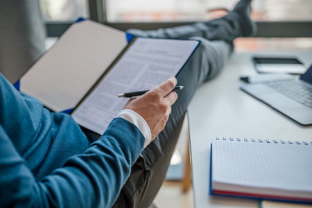 Midsection of male entrepreneur analyzing documents. Close-up of businessman sitting with papers. He is working at desk in corporate workplace.の写真素材