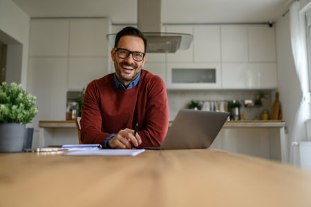 Portrait of smiling handsome businessman with glasses on working over laptop at desk in home officeの写真素材