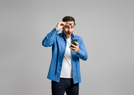 Young businessman looking at his mobile phone with surprise expression isolated over gray backgroundの写真素材