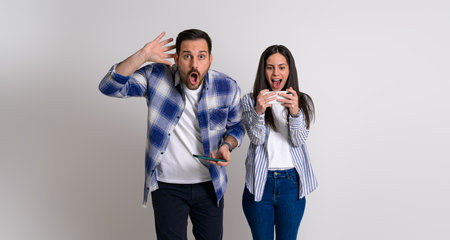 Shocked boyfriend with head in hand looking at camera after losing video game to girlfriend screaming excitedly and celebrating her success. Young gamers with smart phones competing each other on backgroundの写真素材