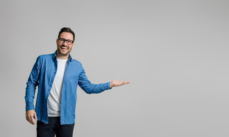 Portrait of cheerful handsome businessman showing and advertising new product on gray backgroundの写真素材