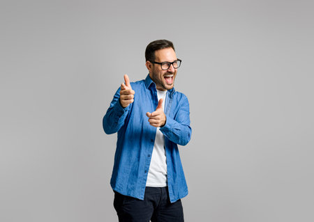 Portrait of handsome cheerful young businessman pointing at camera while posing on gray backgroundの写真素材