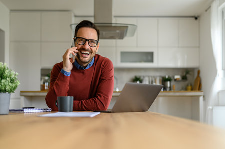 Portrait of happy male entrepreneur making a business call and working on laptop in home officeの写真素材