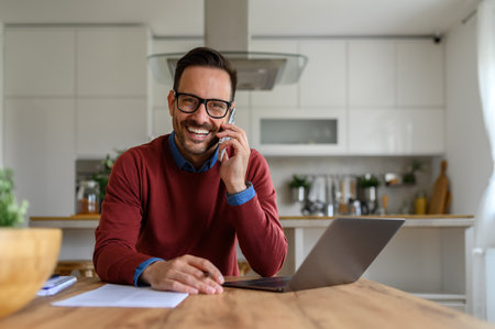 Confident male professional smiling at camera and making business call at desk in home officeの写真素材