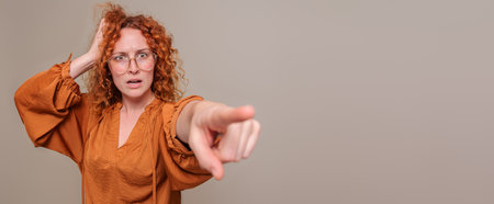 Stressed and worried young businesswoman with hand in hair pointing away against background