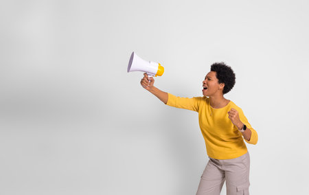 Young female activist holding megaphone and screaming while protesting over white backgroundの写真素材