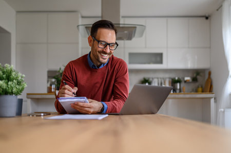 Smiling financial adviser writing notes while discussing over video call on laptop at home officeの写真素材
