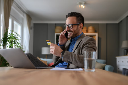 Low angle view of businessman sharing credit card details over phone call while working from homeの写真素材