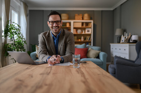 Portrait of happy businessman dressed in elegant suit working over laptop on desk in home officeの写真素材