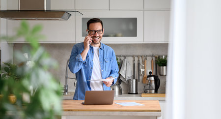 Happy businessman discussing financial report over smart phone while standing at kitchen counterの写真素材