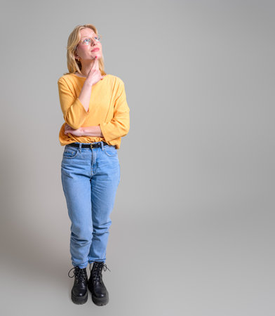 Businesswoman with hand on chin looking away and contemplating while standing on white backgroundの写真素材