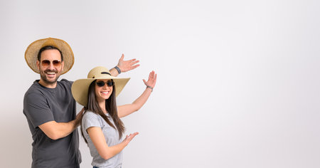 Portrait of smiling young couple wearing sunglasses and hats showing copy space on white backgroundの写真素材