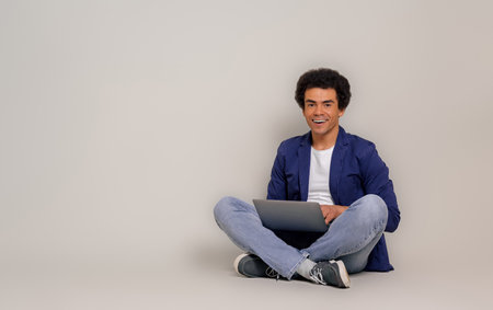 Happy young businessman with afro hair doing research over laptop while sitting on white background