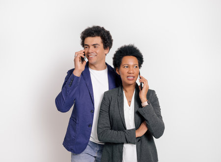 Portrait of professional partners discussing over smart phones while standing on white backgroundの写真素材