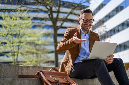 Low angle view of positive businessman discussing over video call on laptop while sitting on stepsの写真素材