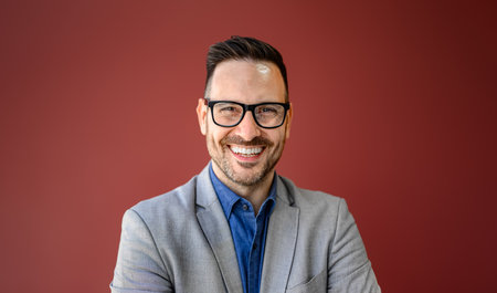 Close-up portrait of smiling young businessman in eyeglasses posing against isolated red backgroundの写真素材
