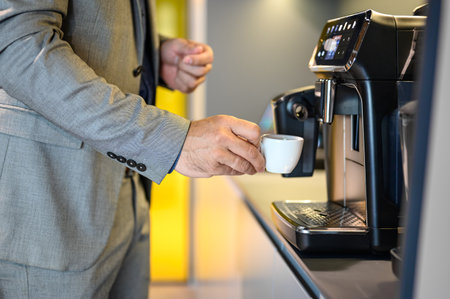 Midsection of businessman holding cup and making coffee in coffeemaker while taking break in office