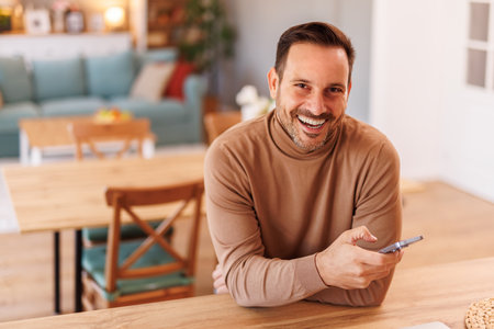 High angle portrait of confident businessman using mobile phone while sitting at desk in home officeの写真素材