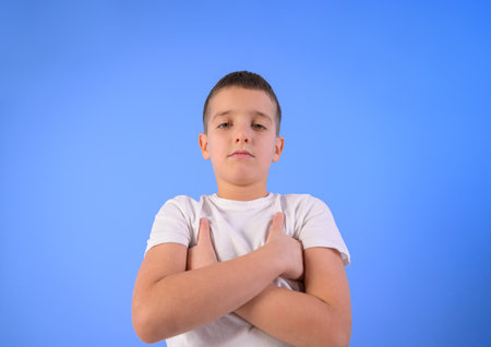 Portrait of confident serious boy with arms crossed standing against isolated blue backgroundの写真素材