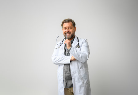 Portrait of smiling male doctor in lab coat with eyeglasses standing against isolated white backgroundの写真素材