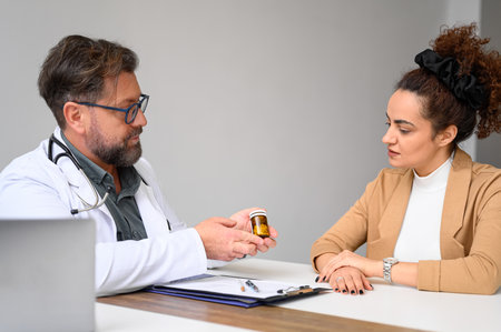Male doctor in lab coat and glasses consulting female patient and giving medications to her in hospitalの写真素材