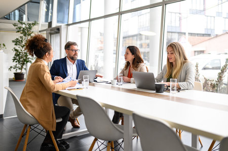 Business professionals with laptops and reports discussing strategies and planning project in...