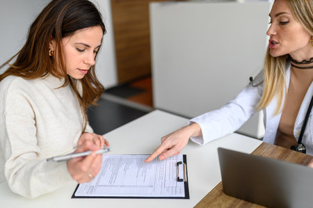 High angle view of female doctor pointing at details while patient filling form on desk during consultationの写真素材