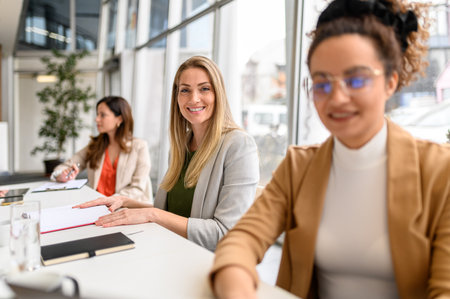 Portrait of confident businesswoman with note pad working with female coworkers in modern board roomの写真素材
