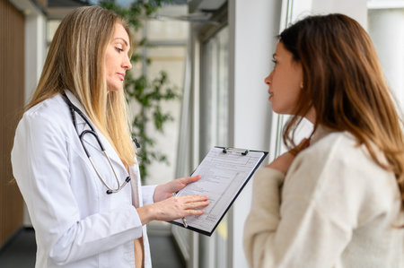 Female doctor in lab coat showing and discussing medical test results with patient in hospital...