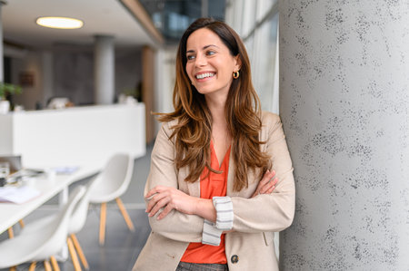 Portrait of confident businesswoman with arms crossed smiling and looking away while standing by...