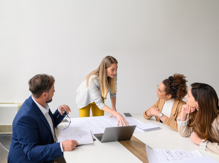 Female engineer reviewing blueprint with colleagues in meeting discussing construction plans and collaborating in officeの写真素材