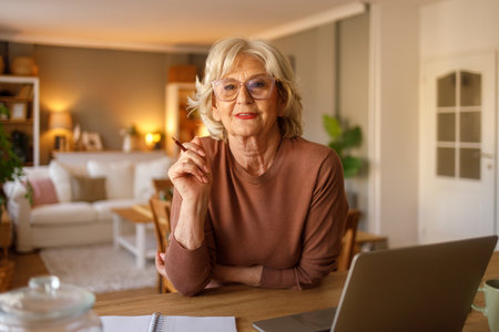 Portrait of confident senior woman using laptop for paying bills and managing digital banking while sitting at homeの写真素材