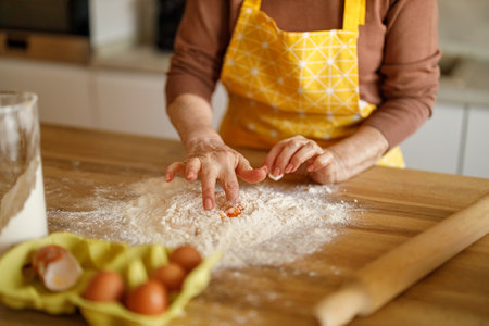 Midsection of senior woman in apron mixing egg yolk and flour on island while blogging about cookie...