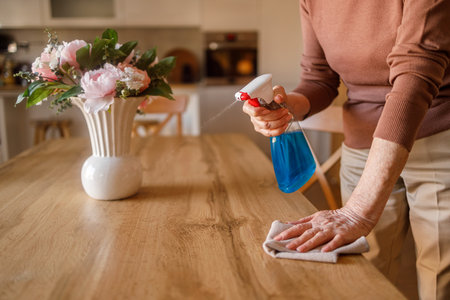 Midsection of senior woman wiping wooden dining table with spray bottle and napkin while doing household choresの写真素材