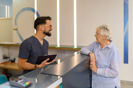 Senior woman talking to male receptionist at desk in hospital during appointment enquiry and vision consultationの写真素材