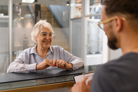 Happy senior woman interacting with male doctor at reception counter during hospital visit for medical guidanceの写真素材