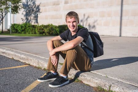 Happy teenager sitting on curb in front of high school.の写真素材