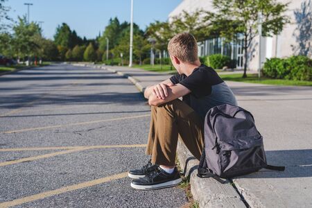 Lonely teenage boy sitting on curb next to high school.の写真素材