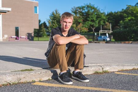 Sad teenage boy sitting on the curb in front of his school.の写真素材