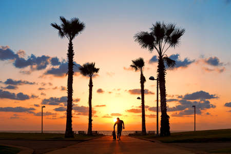 man running with skateboard near the ocean in sunsetの写真素材