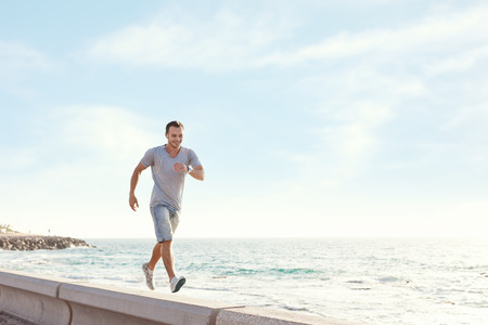 young man walking over the pier near the ocean with earphones and musicの写真素材