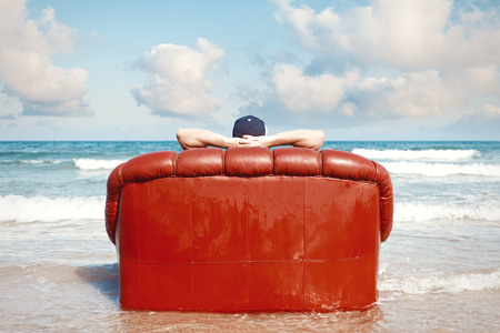 man resting in leather couch on the beach