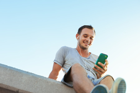 young and handsome man with mobile smartphone sitting on the benchの写真素材