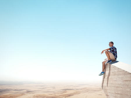 Young man sitting on a cliff and looking at the desertの写真素材