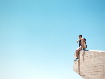 Young man sitting on a cliff at sunny dayの写真素材