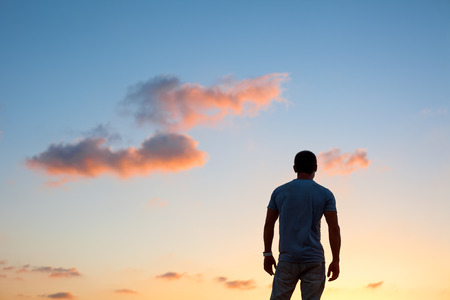 young man silhouette standing at sunset at duskの写真素材