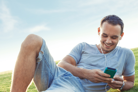 young and handsome man with mobile smartphone lying in the parkの写真素材