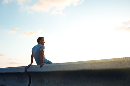 young man sitting sitting at sunset at duskの写真素材