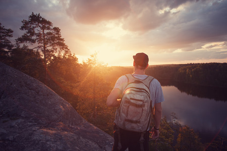 Young casual man on the cliff above river and looking far away at sunsetの写真素材