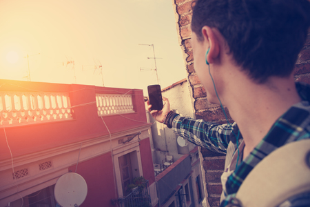 Brave young traveler man doing photo with mobile phone on the roofの写真素材